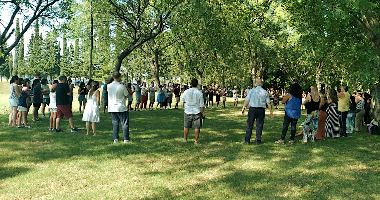 A la sombra de los árboles del parque Taborin, un grupo grande de funcionarios del colegio, de pie y en una ronda, siguen las indicaciones de Alejandro Venossa que, micrófono en mano, dirige el momento.